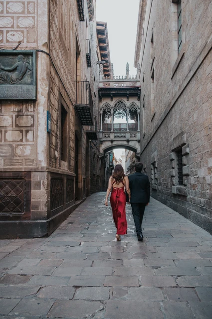A walk beneath Pont del Bisbe | Barcelona engagement photoshoot The couple walking together along the stone lane beneath Pont del Bisbe in the Gothic Quarter during their engagement photoshoot in Barcelona.