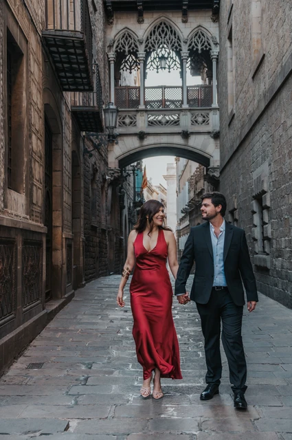 The couple walking together along the stone lane beneath Pont del Bisbe in the Gothic Quarter during their engagement photoshoot in Barcelona.