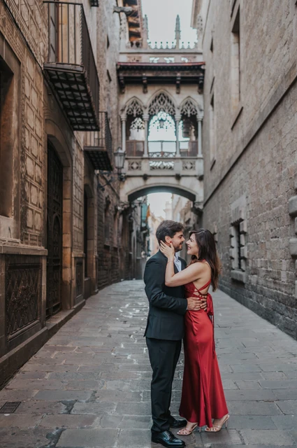 Close together beneath Pont del Bisbe | Barcelona engagement photoshoot The couple standing close together beneath Pont del Bisbe, framed by the Gothic Quarter’s old stone buildings during their engagement photoshoot in Barcelona.