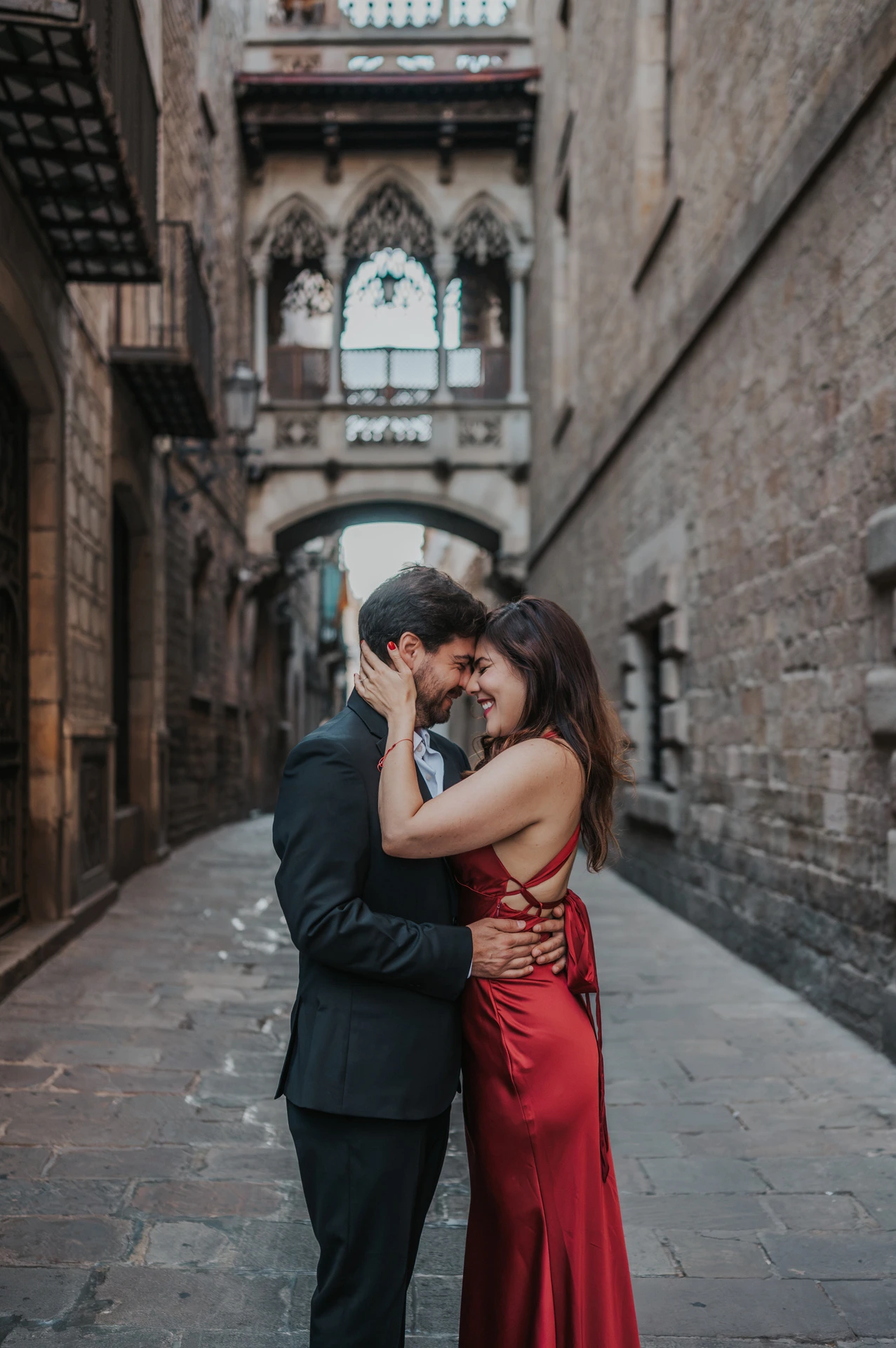 The couple standing close together beneath Pont del Bisbe, framed by the Gothic Quarter’s old stone buildings during their engagement photoshoot in Barcelona.
