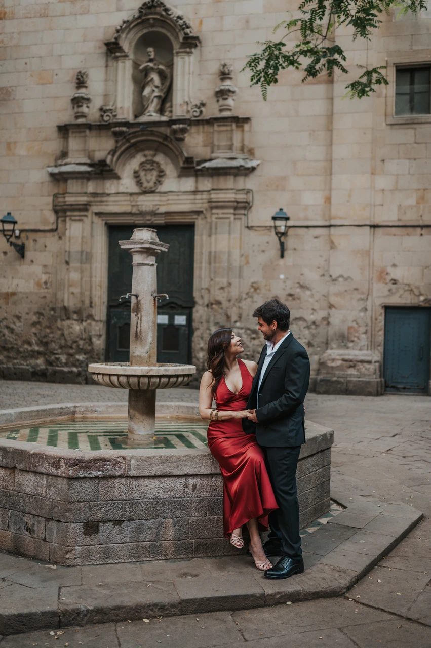 A portrait beside the fountain in Plaça de Sant Felip Neri | Barcelona engagement photoshoot The couple beside the stone fountain in Plaça de Sant Felip Neri, with the church façade behind them during their engagement photoshoot in Barcelona.