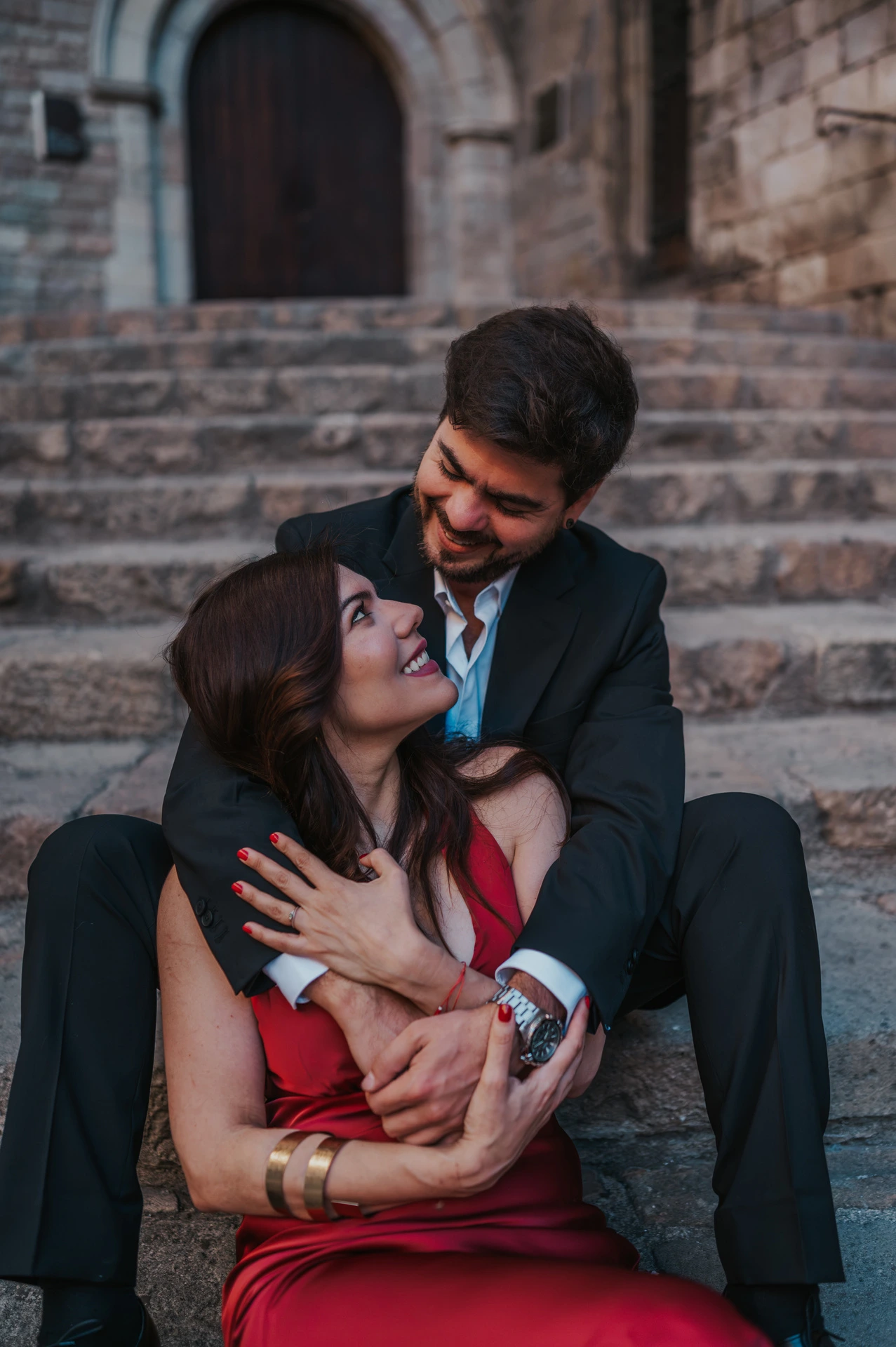 The couple sitting close together on the stone steps at Plaça del Rei, beneath an arched doorway during their engagement photoshoot in Barcelona.