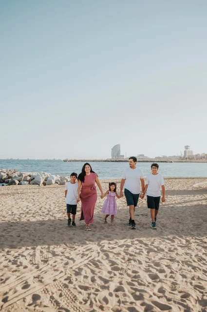 A family walk across the sand | Barcelona family photoshoot The family walking together across the sand, with the sea and W Hotel behind them during their family photoshoot in Barcelona.