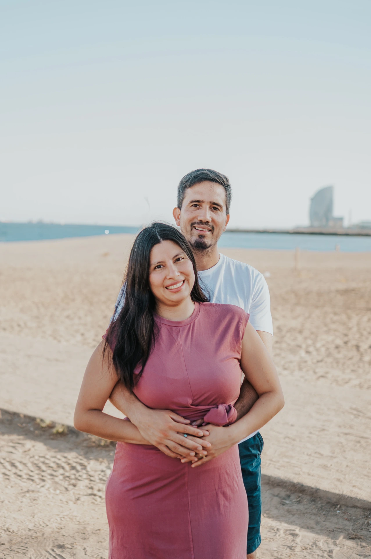 The parents embracing on the sand, with the sea and W Hotel behind them during their family photoshoot in Barcelona.