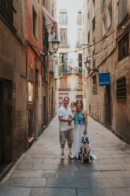 A street portrait with the family dog in El Born | Barcelona family photoshoot The parents holding their toddler with their dog sitting beside them on an El Born street during their family photoshoot in Barcelona.