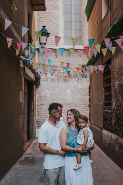 Family portraits beneath colourful bunting in El Born | Barcelona family photoshoot The parents standing close together with their toddler beneath colourful bunting in an El Born lane during their family photoshoot in Barcelona.