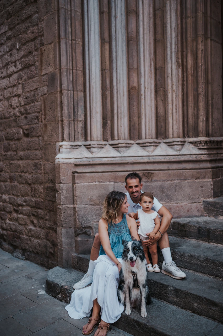 Family portraits with the dog on the stone steps in El Born | Barcelona family photoshoot The family sitting on stone steps with their dog in front of them beside a tall carved doorway in El Born during their family photoshoot in Barcelona.