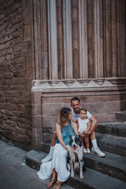 Family portraits with the dog on the stone steps in El Born | Barcelona family photoshoot The family sitting on stone steps with their dog in front of them beside a tall carved doorway in El Born during their family photoshoot in Barcelona.