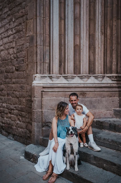 The family sitting on stone steps with their dog in front of them beside a tall carved doorway in El Born during their family photoshoot in Barcelona.