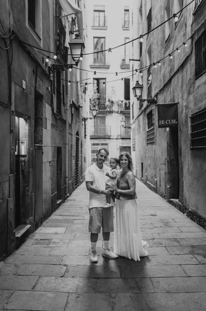 Together in an El Born lane in black and white | Barcelona family photoshoot Black-and-white photograph: the parents holding their toddler together in a narrow El Born lane lined with balconies during their family photoshoot in Barcelona.