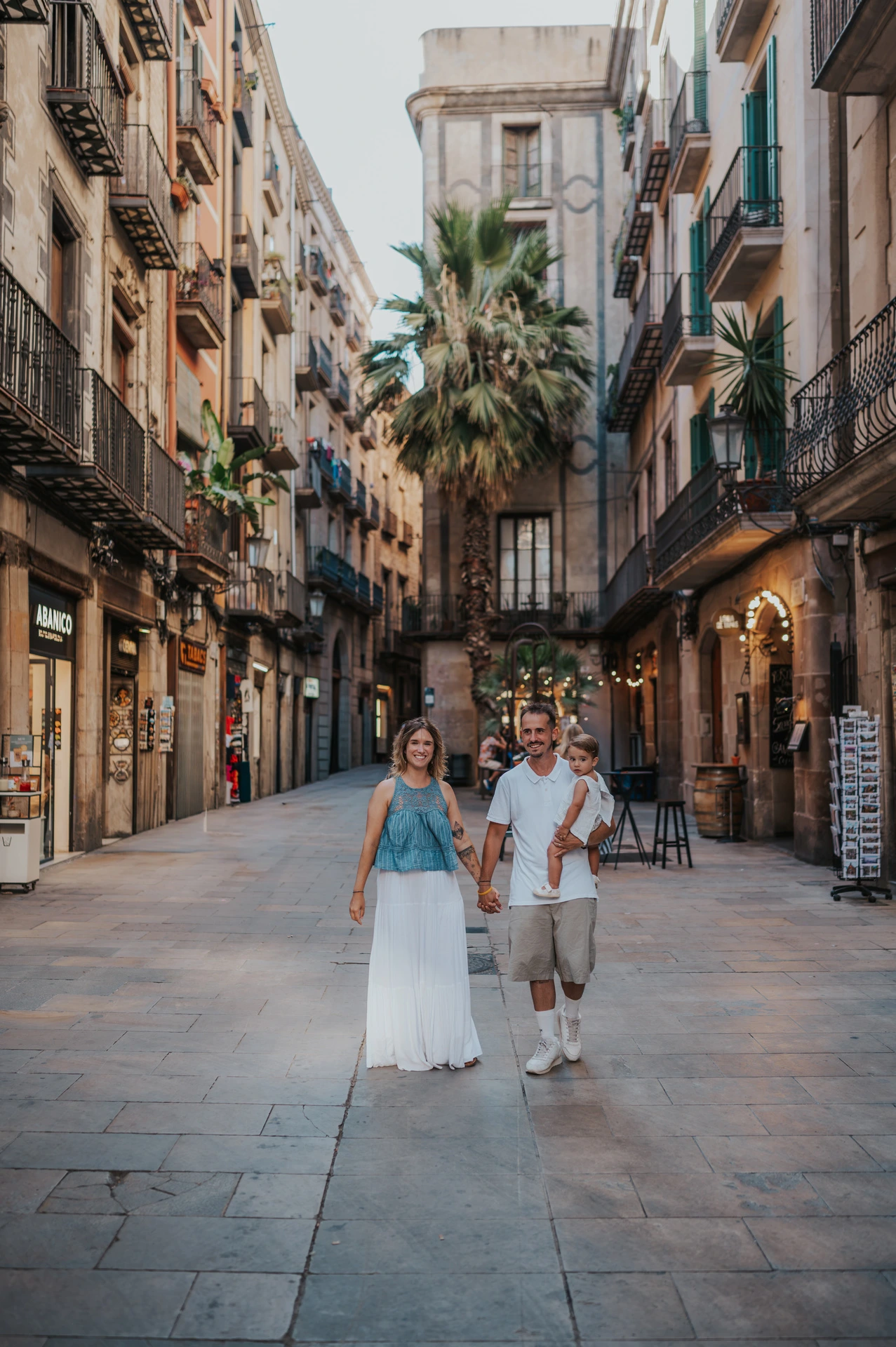 The parents walking hand in hand along a shop-lined street in El Born during their family photoshoot in Barcelona.