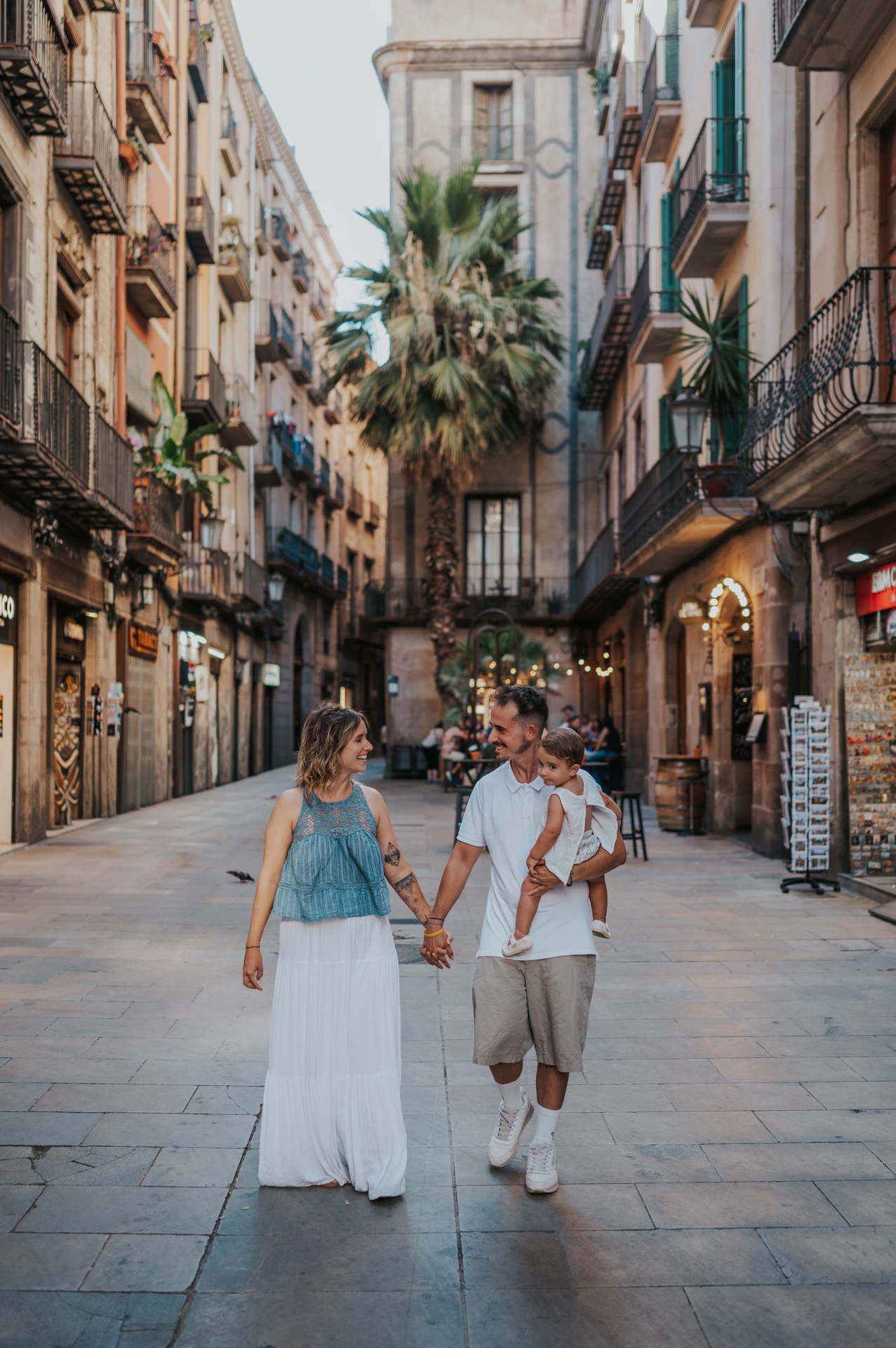 The parents walking hand in hand along a shop-lined street in El Born during their family photoshoot in Barcelona.