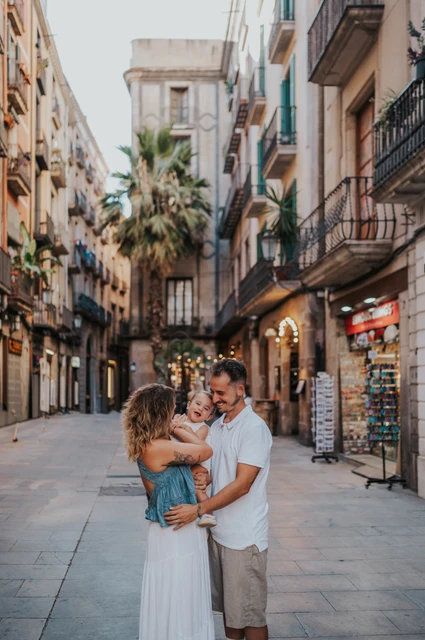 A cuddle in the streets of El Born | Barcelona family photoshoot The parents holding their toddler close together on an El Born street with balconies and palm trees during their family photoshoot in Barcelona.