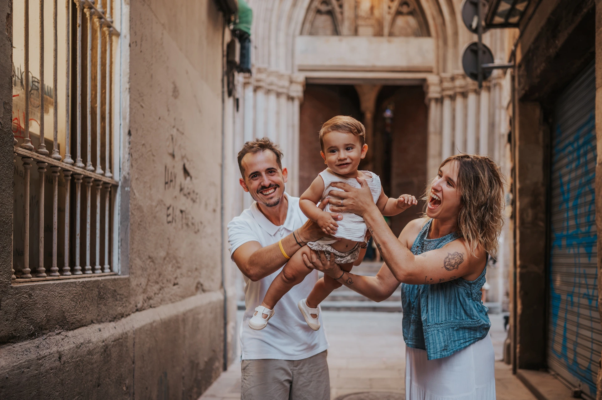 The parents holding their smiling toddler between them in an El Born passage during their family photoshoot in Barcelona.
