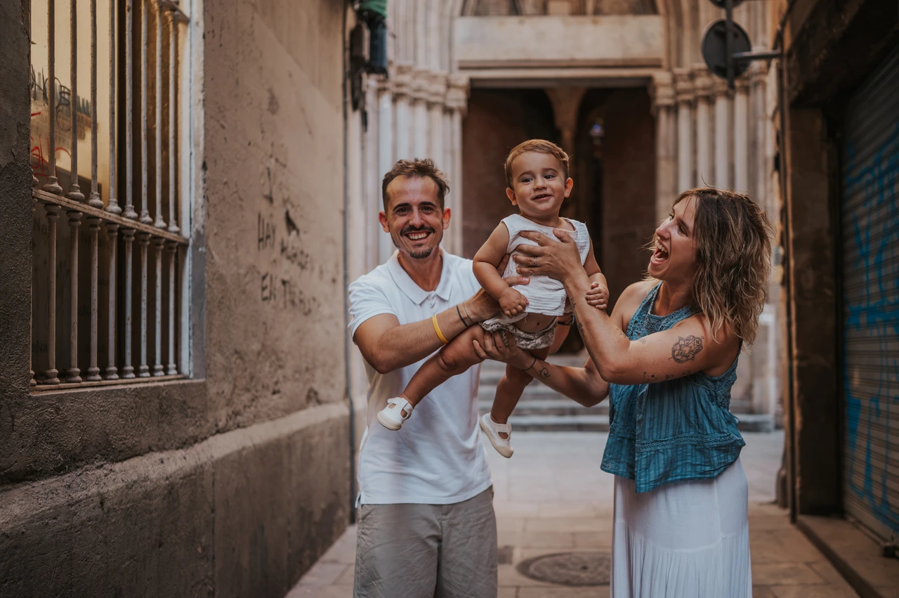 A smiling toddler between the parents in El Born | Barcelona family photoshoot The parents holding their smiling toddler between them in an El Born passage during their family photoshoot in Barcelona.