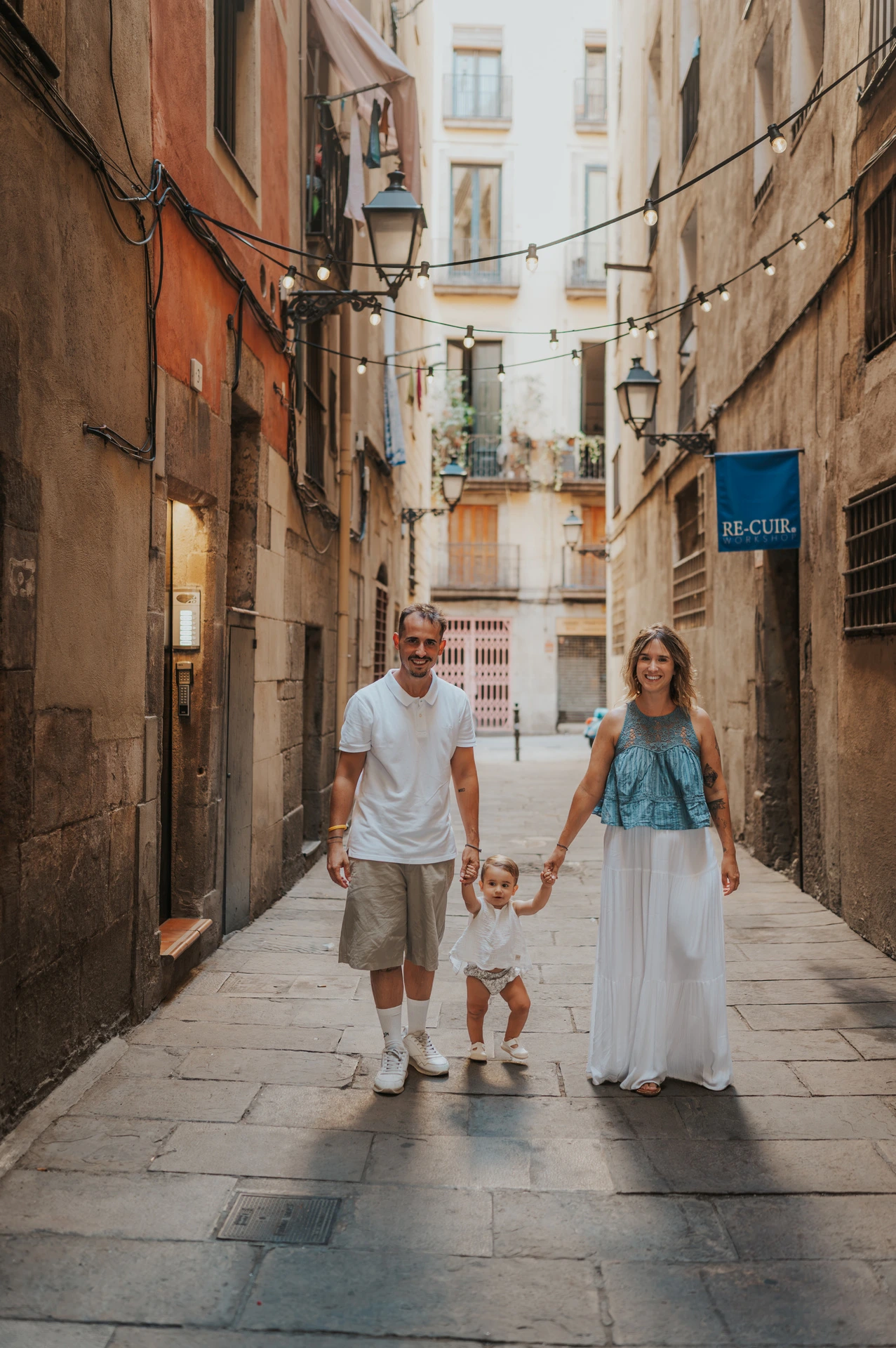 The toddler walking between the parents and holding their hands on an El Born street during their family photoshoot in Barcelona.