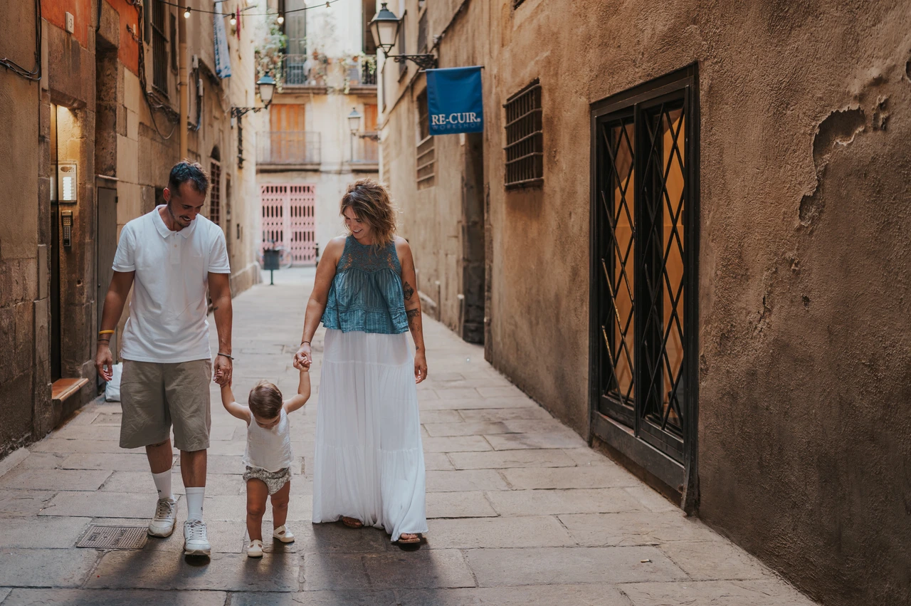 A hand-in-hand family walk in El Born | Barcelona family photoshoot The toddler walking between the parents and holding their hands on an El Born street during their family photoshoot in Barcelona.