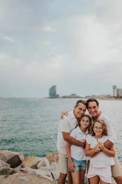 A family hug by the sea | Barcelona family photoshoot The parents and their two daughters gathered together in a close embrace beside the sea during their family photoshoot in Barcelona.