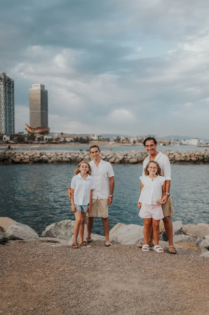Family photographs hand in hand by the sea | Barcelona family photoshoot The parents and their two daughters standing together and holding hands beside the sea during their family photoshoot in Barcelona.