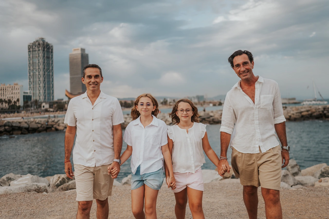 Family photographs hand in hand by the sea | Barcelona family photoshoot The parents and their two daughters standing together and holding hands beside the sea during their family photoshoot in Barcelona.