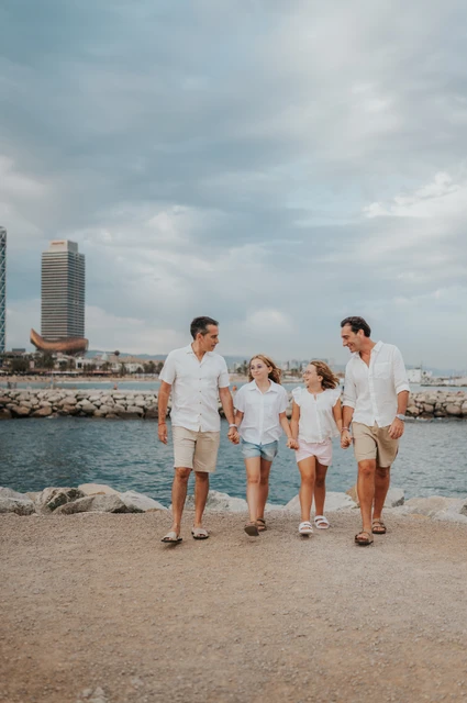 Family photographs hand in hand by the sea | Barcelona family photoshoot The parents and their two daughters standing together and holding hands beside the sea during their family photoshoot in Barcelona.