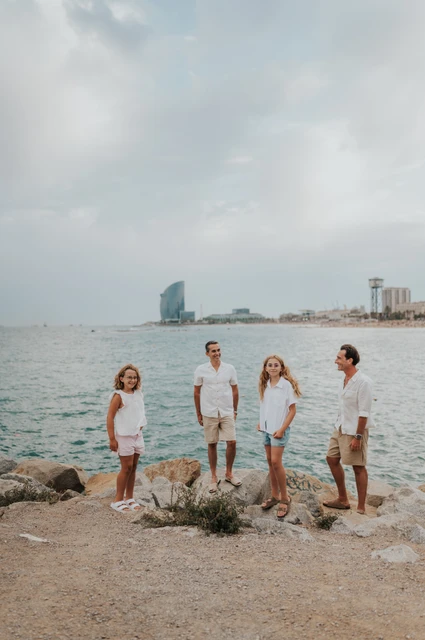 Family portraits against the Barcelona seafront | Barcelona family photoshoot The family of four gathered on the rocky shoreline, with the open sea and W hotel beyond them during their family photoshoot in Barcelona.