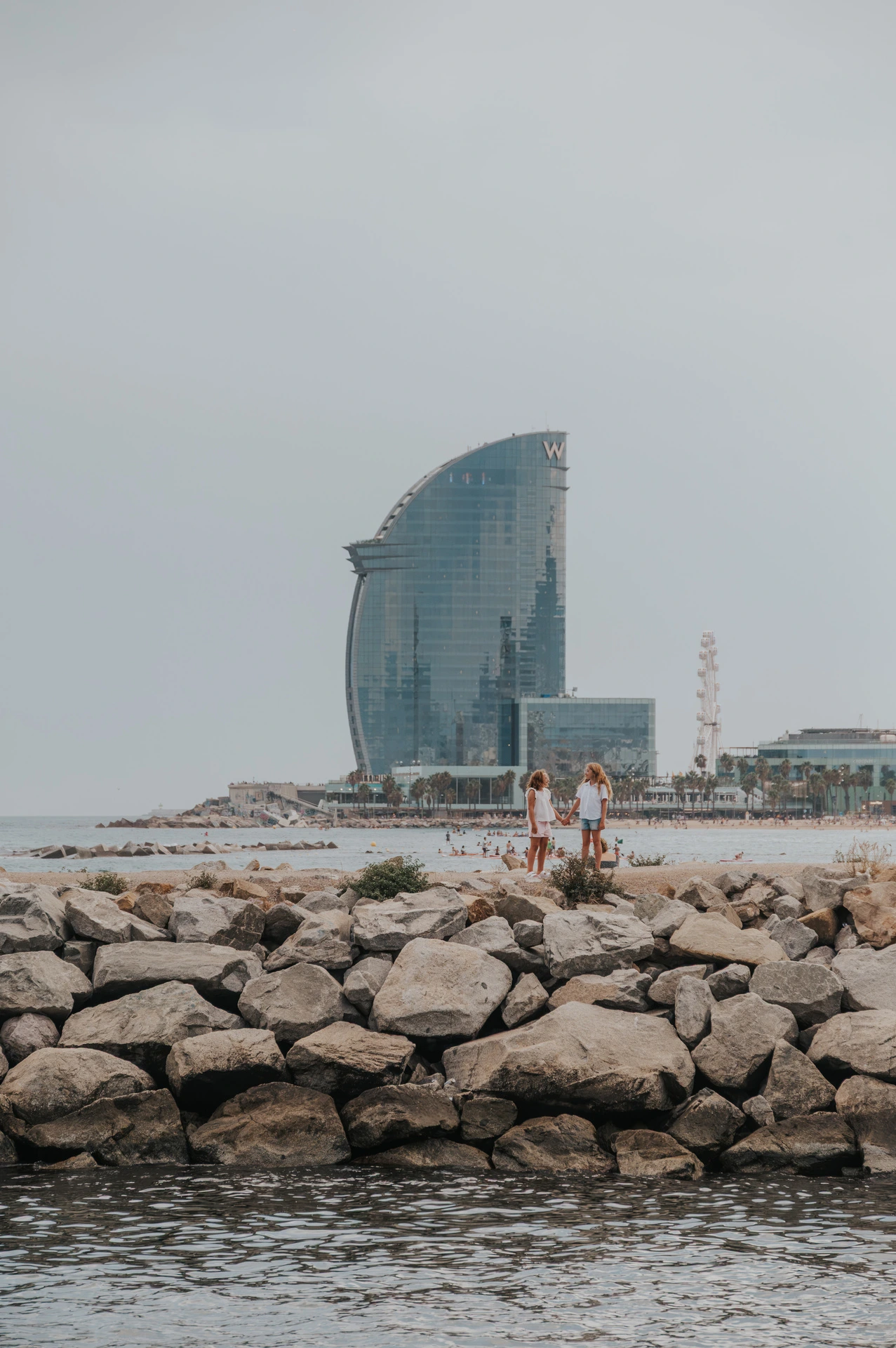 The family together on the rocky waterfront with the W hotel rising behind them during their family photoshoot in Barcelona.