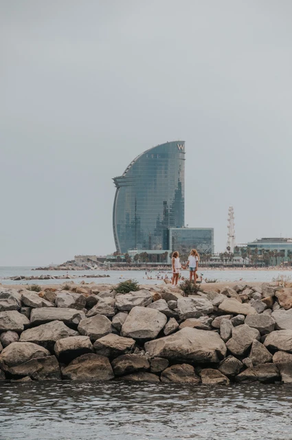 A waterfront family moment beside the W hotel | Barcelona family photoshoot The family together on the rocky waterfront with the W hotel rising behind them during their family photoshoot in Barcelona.