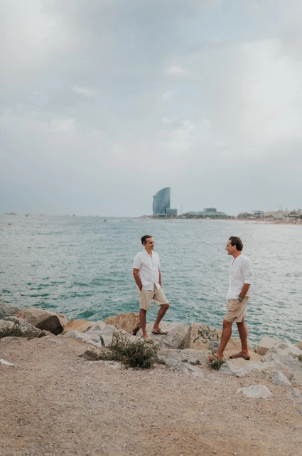 A moment for the parents beside the sea | Barcelona family photoshoot The two parents standing apart on the rocky shoreline and turning towards each other during their family photoshoot in Barcelona.