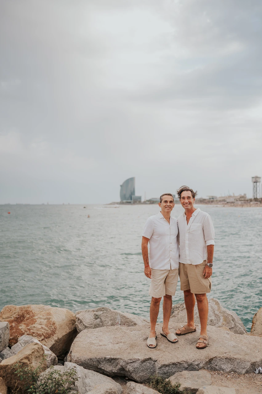 A portrait of the parents by the sea | Barcelona family photoshoot The two parents standing together beside the water and rocky shoreline during their family photoshoot in Barcelona.