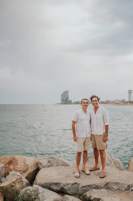 A portrait of the parents by the sea | Barcelona family photoshoot The two parents standing together beside the water and rocky shoreline during their family photoshoot in Barcelona.