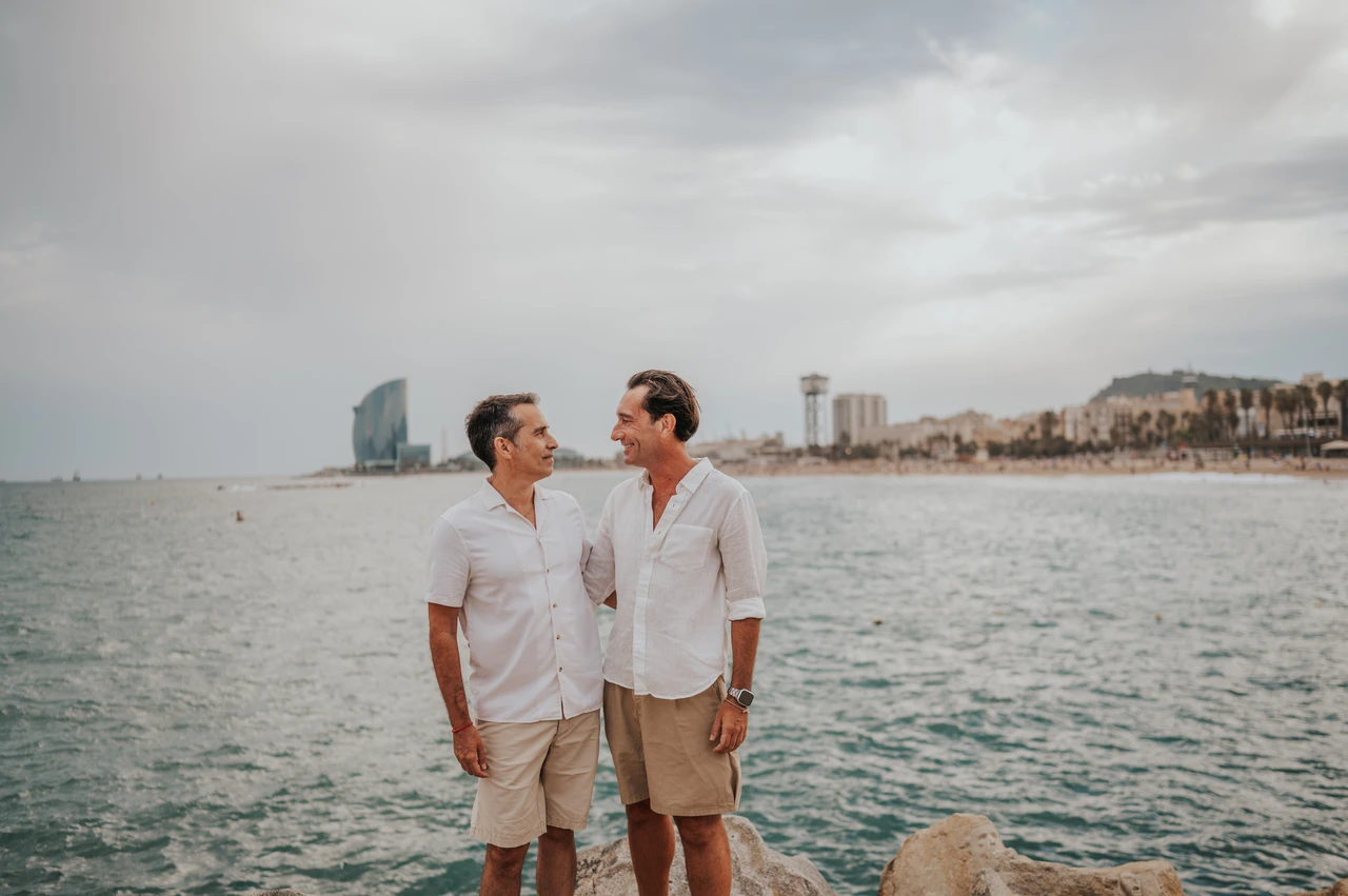 A portrait of the parents by the sea | Barcelona family photoshoot The two parents standing together beside the water and rocky shoreline during their family photoshoot in Barcelona.