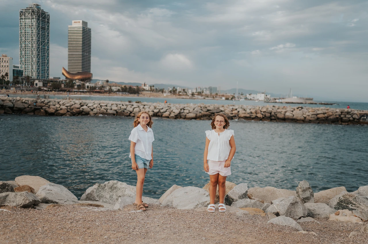 Sisters beside the rocky shoreline | Barcelona family photoshoot The two sisters standing apart on the waterfront path beside the rocks and sea during their family photoshoot in Barcelona.