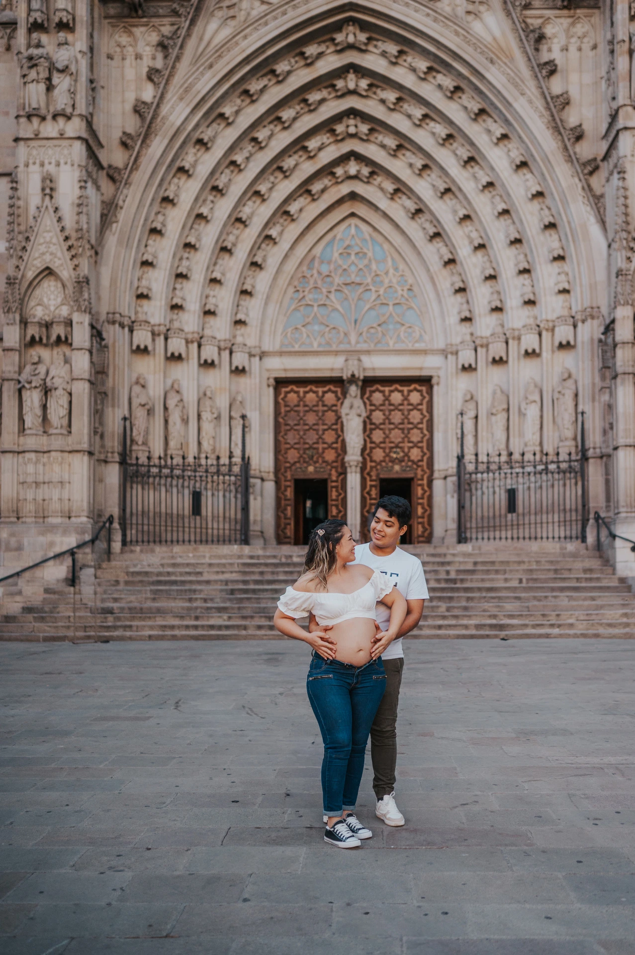 The couple standing close together in front of the cathedral’s carved entrance during their maternity photoshoot in Barcelona.