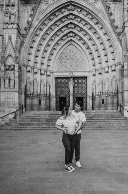 Together in front of the carved cathedral entrance in black and white | Barcelona maternity photoshoot Black-and-white photograph: the couple standing close together in front of the cathedral’s carved entrance during their maternity photoshoot in Barcelona.