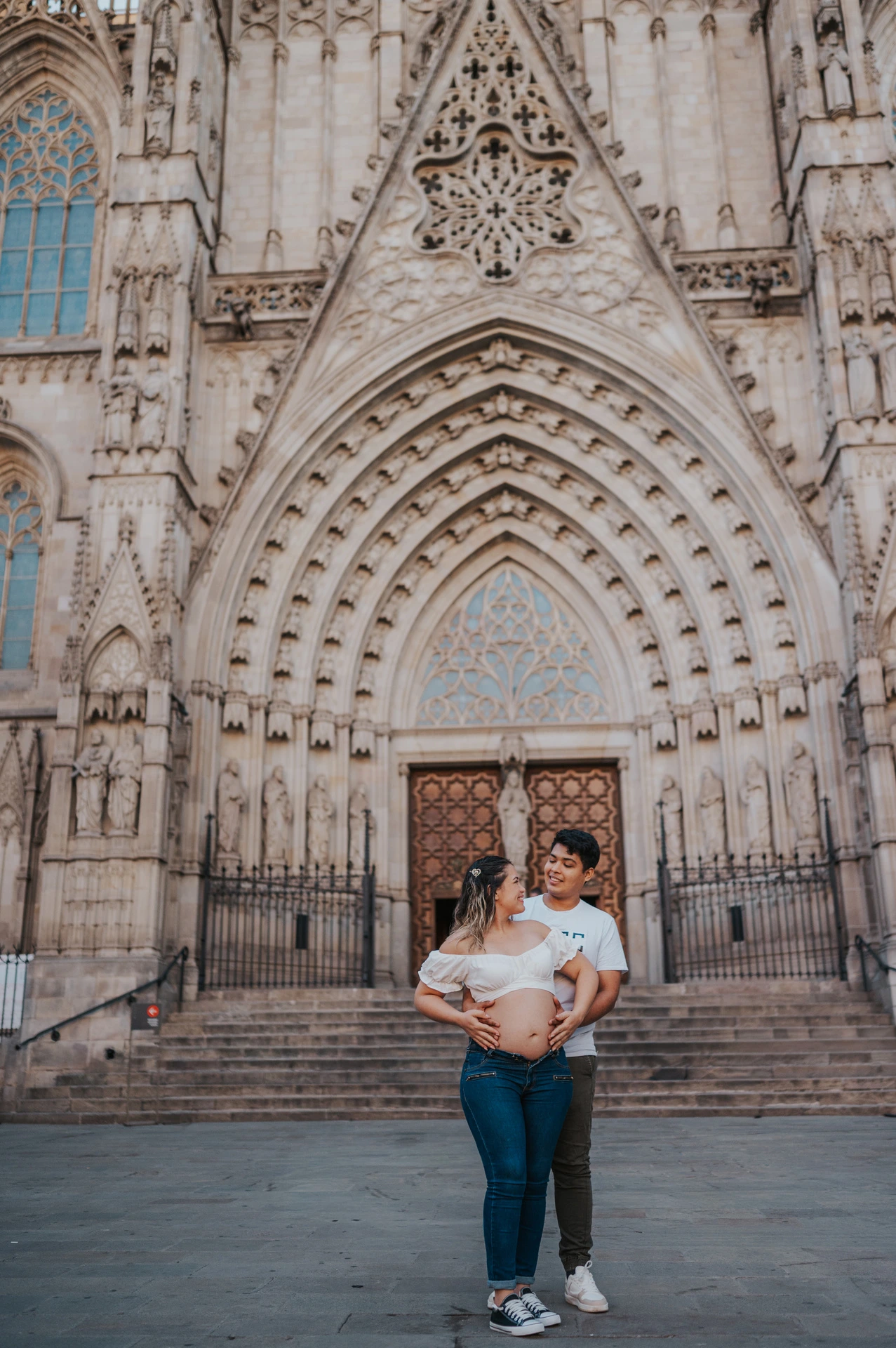 The couple standing close together in front of the cathedral’s carved entrance during their maternity photoshoot in Barcelona.