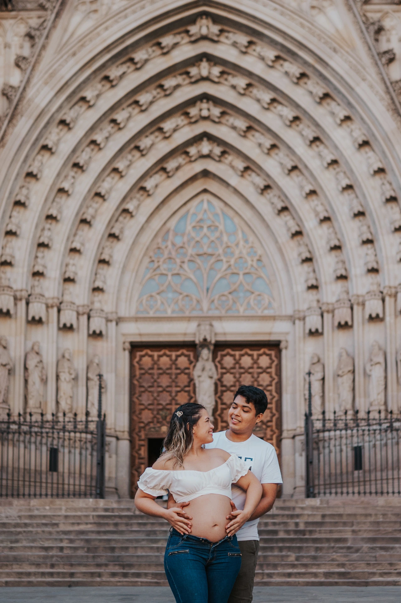 The couple standing close together in front of the cathedral’s carved entrance during their maternity photoshoot in Barcelona.