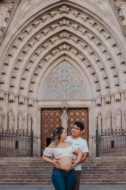 Together in front of the carved cathedral entrance | Barcelona maternity photoshoot The couple standing close together in front of the cathedral’s carved entrance during their maternity photoshoot in Barcelona.