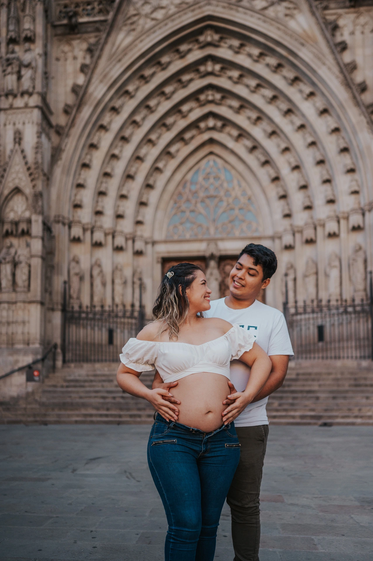 The couple standing close together in front of the cathedral’s carved entrance during their maternity photoshoot in Barcelona.