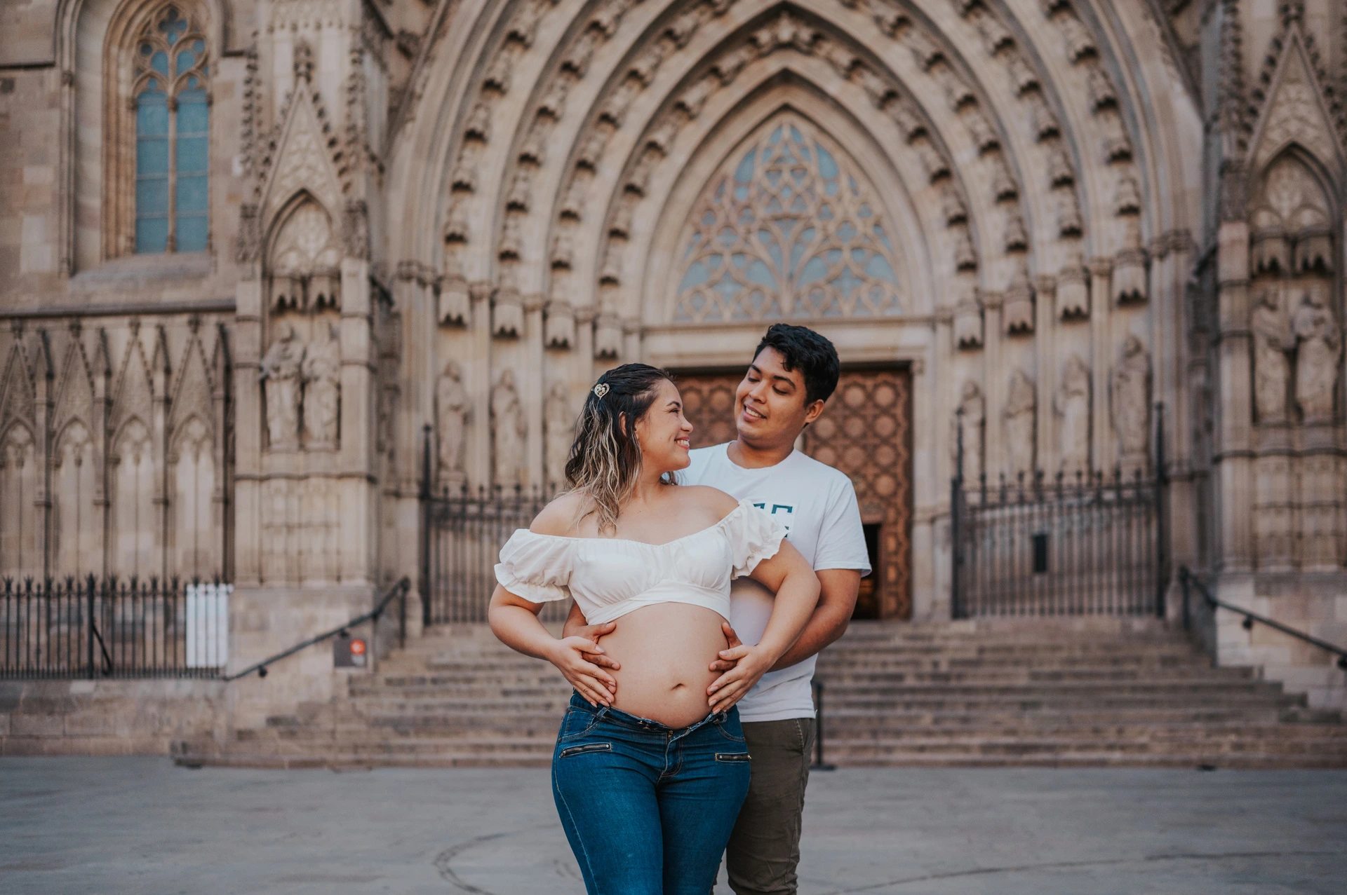 The couple standing close together in front of the cathedral’s carved entrance during their maternity photoshoot in Barcelona.