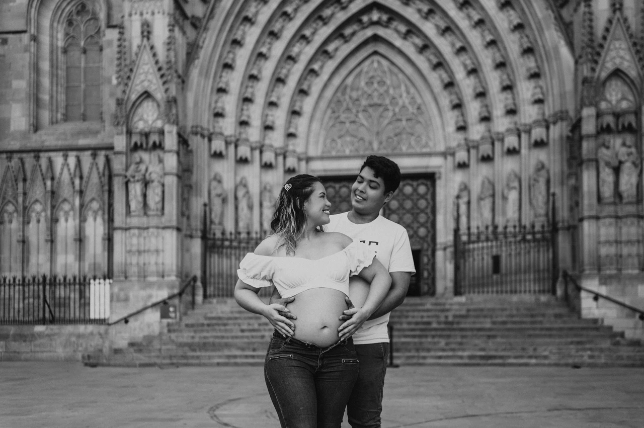 Together in front of the carved cathedral entrance in black and white | Barcelona maternity photoshoot Black-and-white photograph: the couple standing close together in front of the cathedral’s carved entrance during their maternity photoshoot in Barcelona.