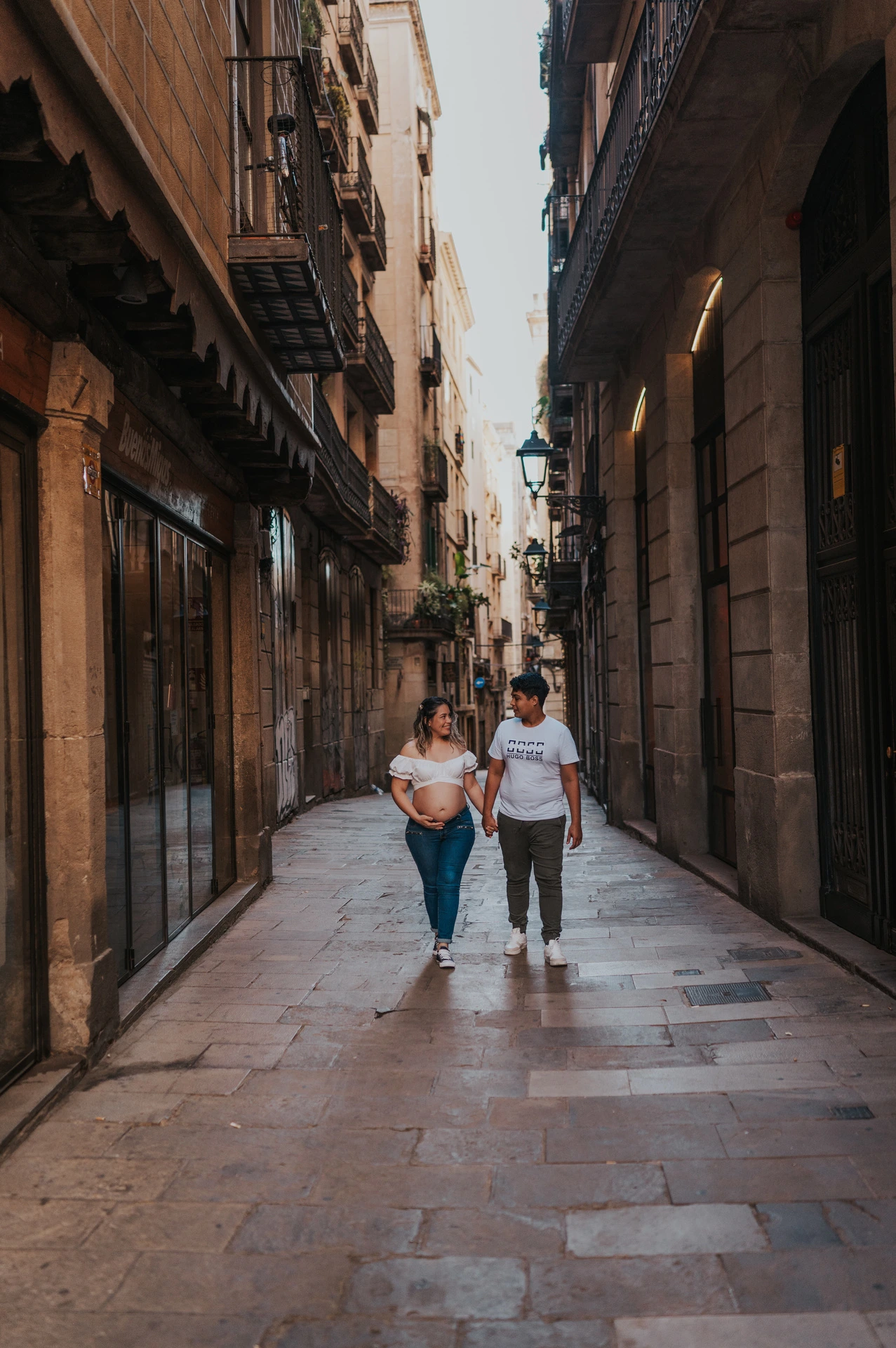 The couple walking together along a narrow street lined with old buildings during their maternity photoshoot in Barcelona.