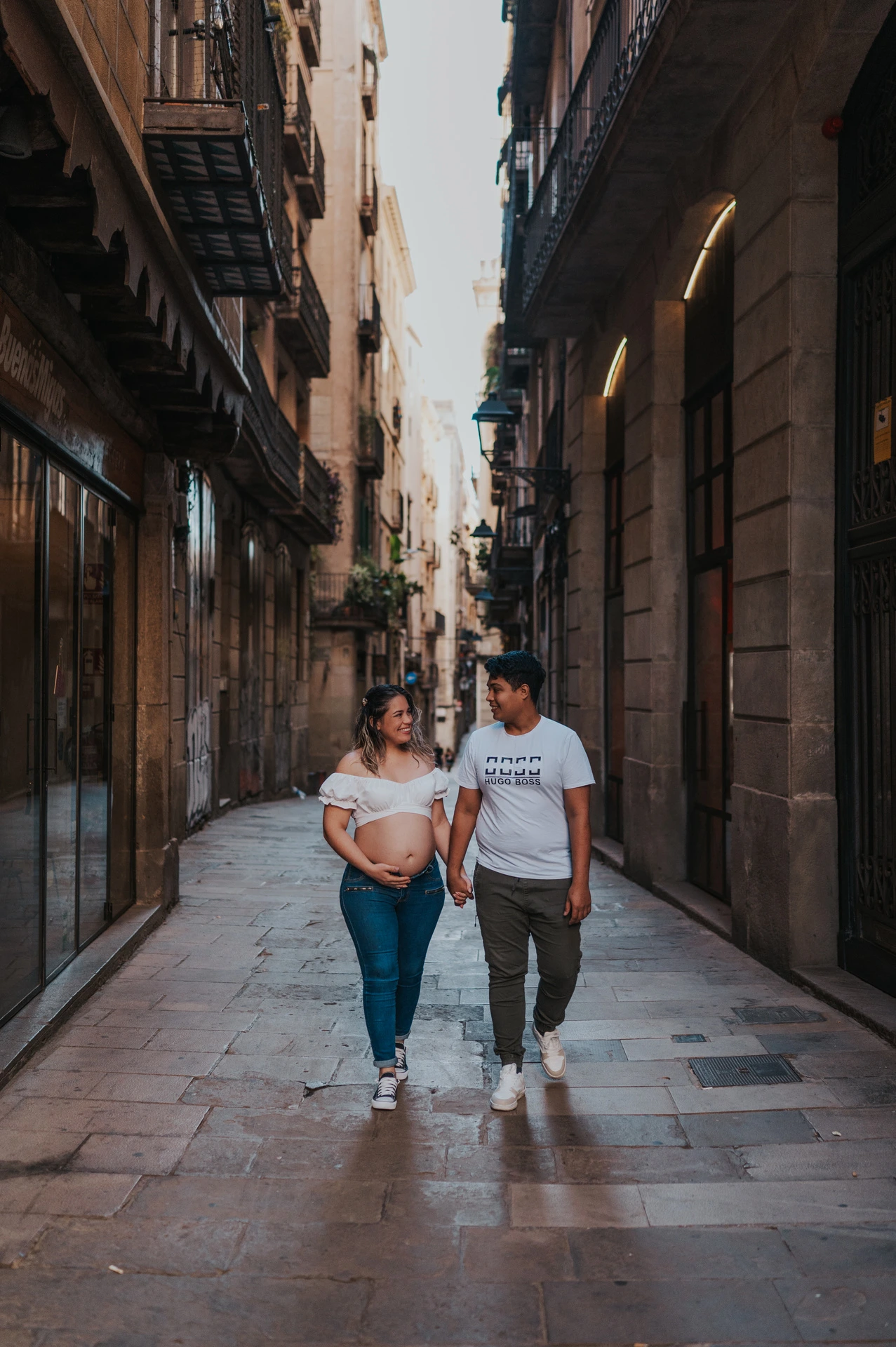 The couple walking together along a narrow street lined with old buildings during their maternity photoshoot in Barcelona.