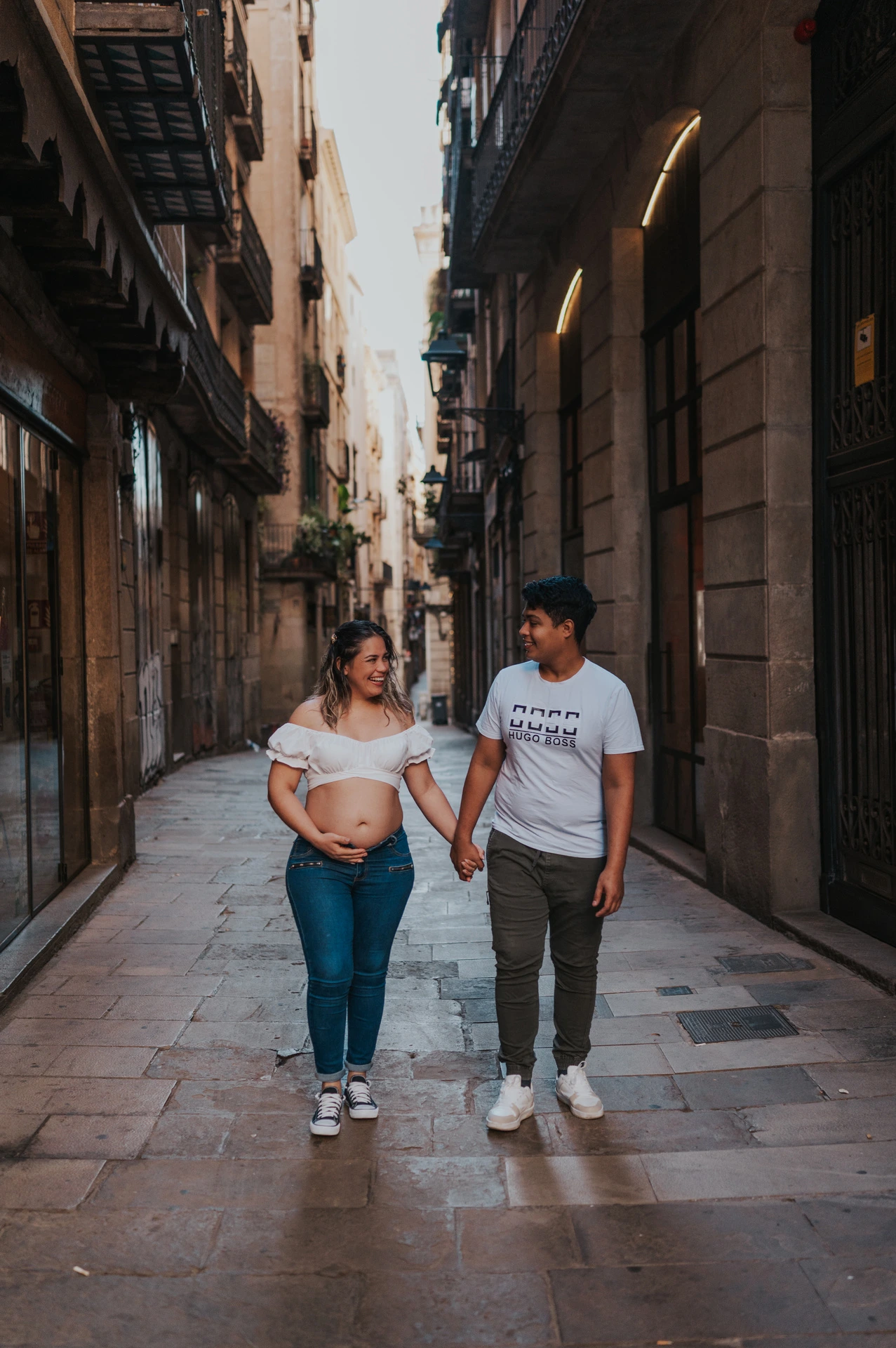 The couple walking together along a narrow street lined with old buildings during their maternity photoshoot in Barcelona.