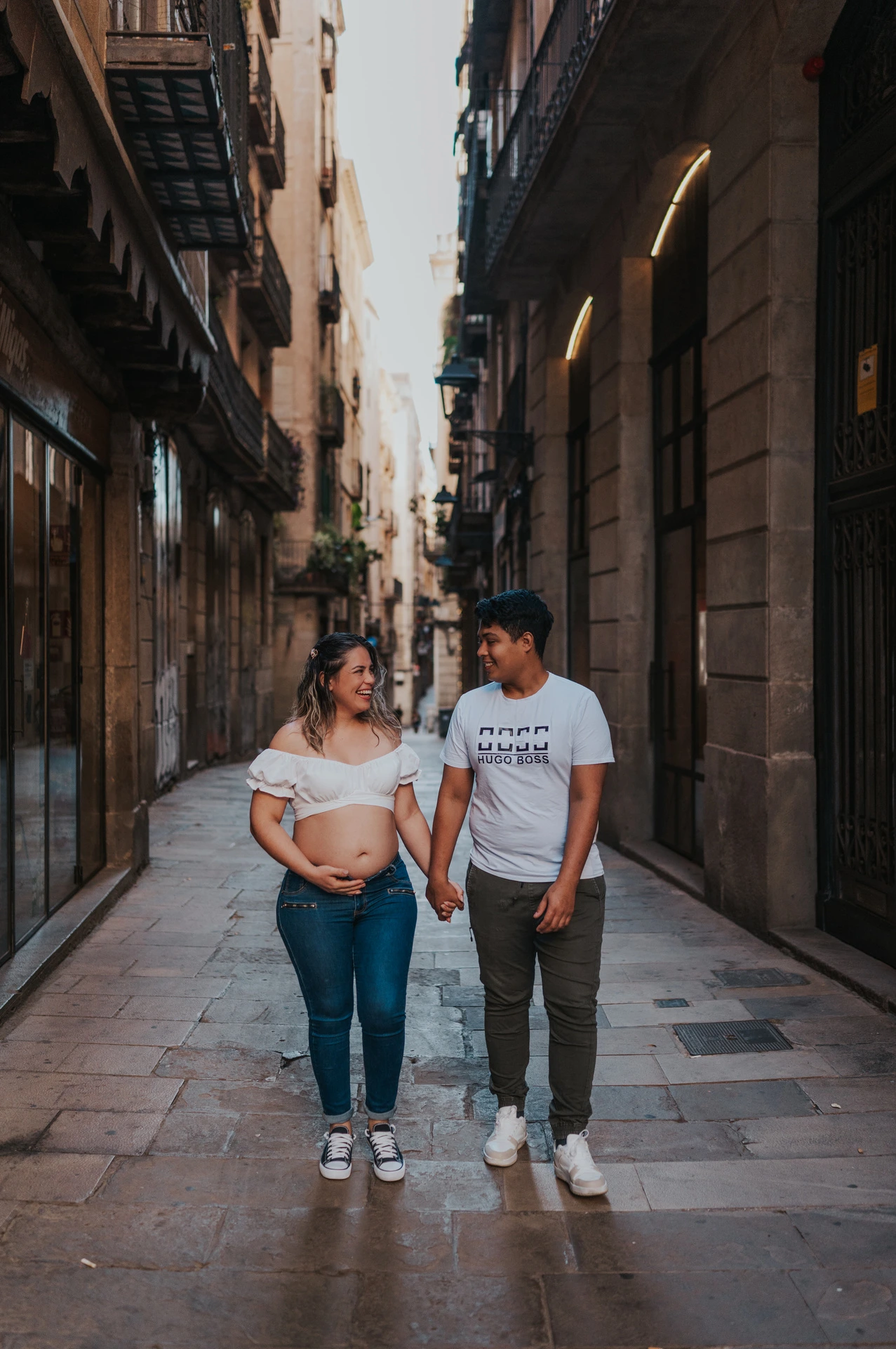 The couple walking together along a narrow street lined with old buildings during their maternity photoshoot in Barcelona.
