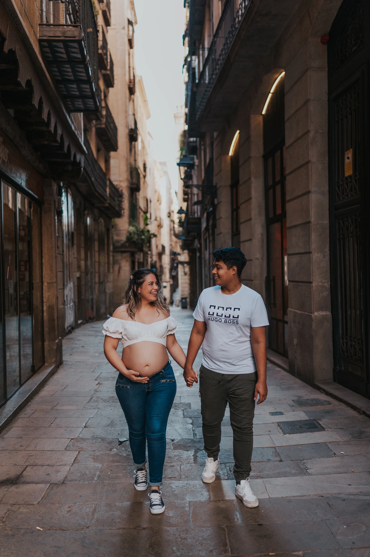 The couple walking together along a narrow street lined with old buildings during their maternity photoshoot in Barcelona.