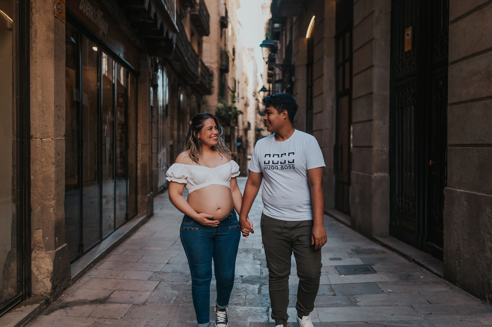 The couple walking together along a narrow street lined with old buildings during their maternity photoshoot in Barcelona.
