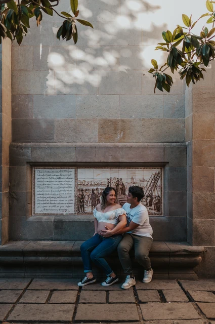 A moment together on the stone bench | Barcelona maternity photoshoot The couple sitting close together on a stone bench beneath a tree during their maternity photoshoot in Barcelona.