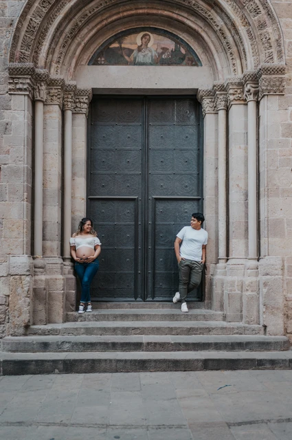 Together beside the carved stone doorway | Barcelona maternity photoshoot The couple standing on either side of a large doorway framed by carved stone and steps during their maternity photoshoot in Barcelona.