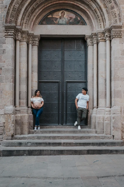 Together beside the carved stone doorway | Barcelona maternity photoshoot The couple standing on either side of a large doorway framed by carved stone and steps during their maternity photoshoot in Barcelona.